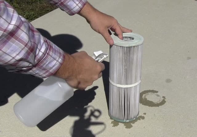 Spraying a hot tub filter with a filter cleaner