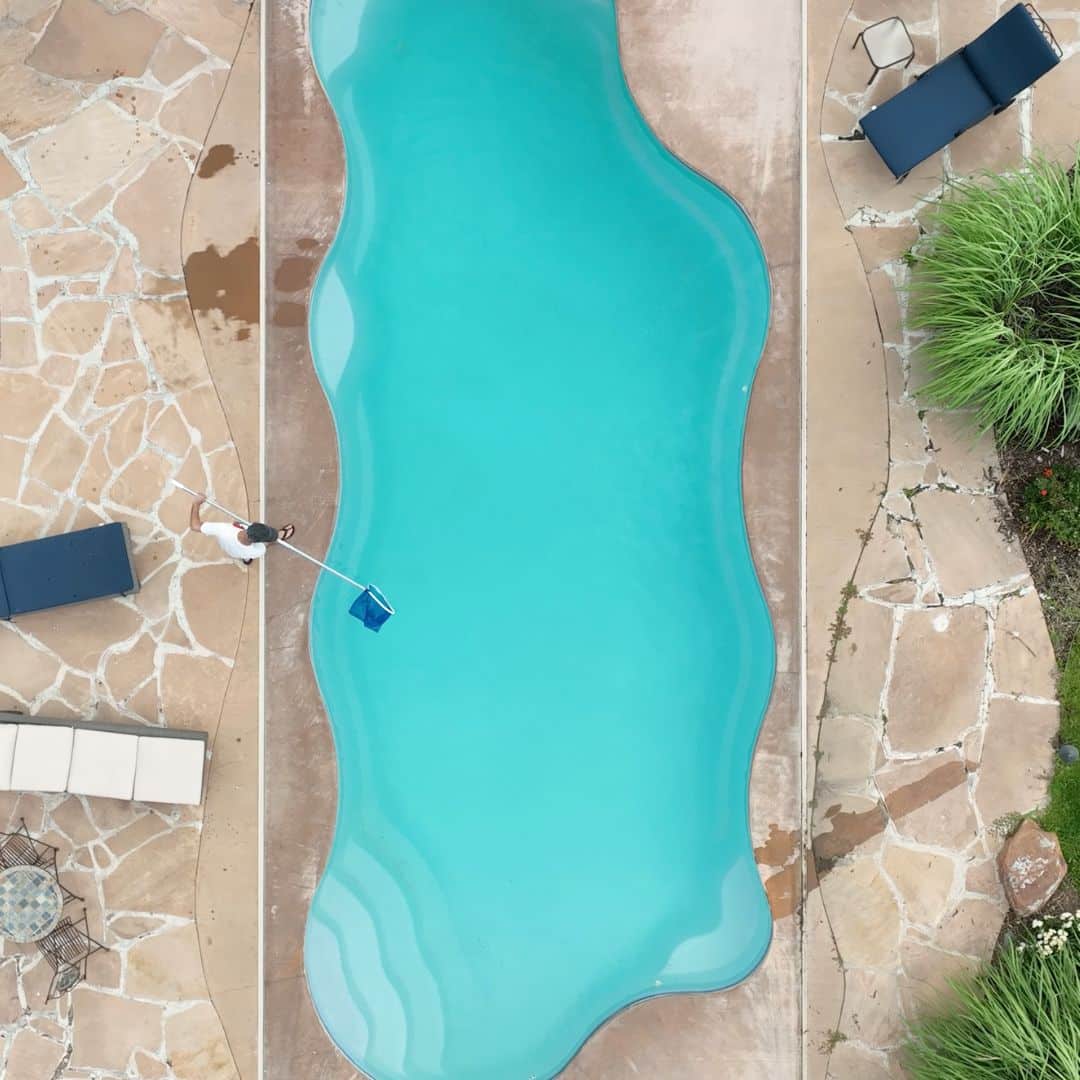 Drone Shot of Man Skimming an Inground Pool