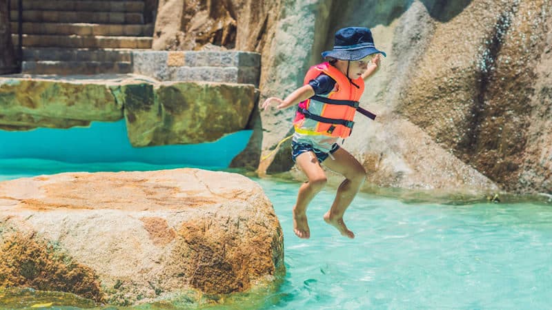 Boy jumping off a stone platform into a pool